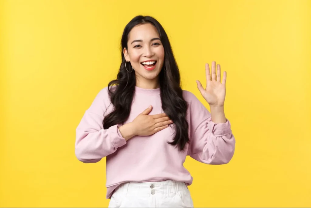Woman smiling, waving against yellow background.