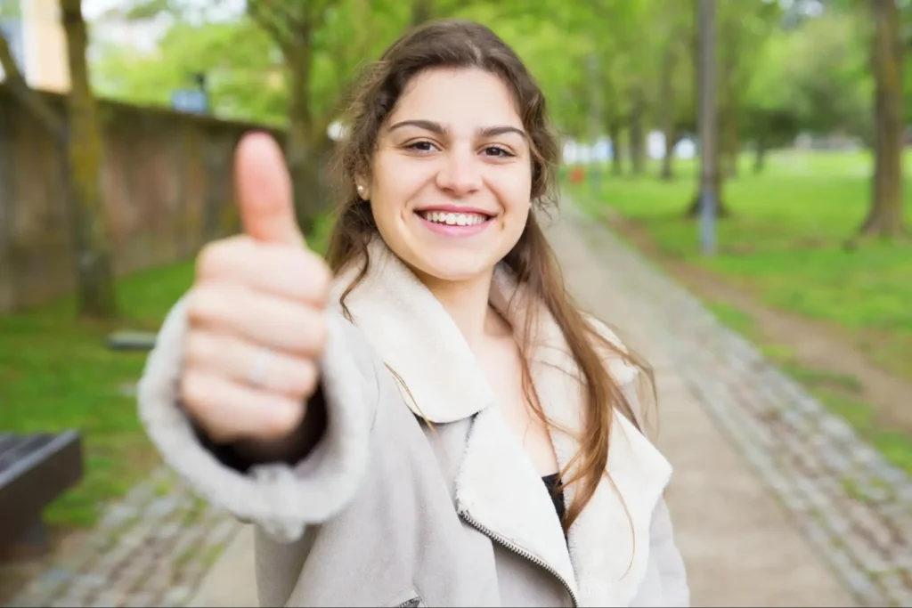 "Smiling woman giving thumbs up outdoors"