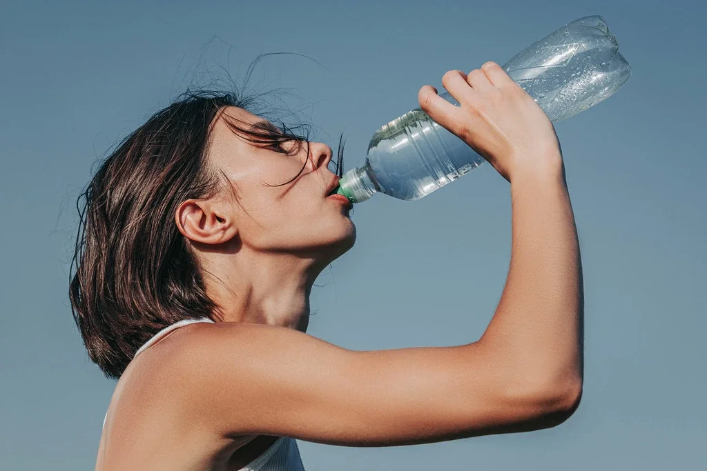 Woman drinking water from bottle outside.